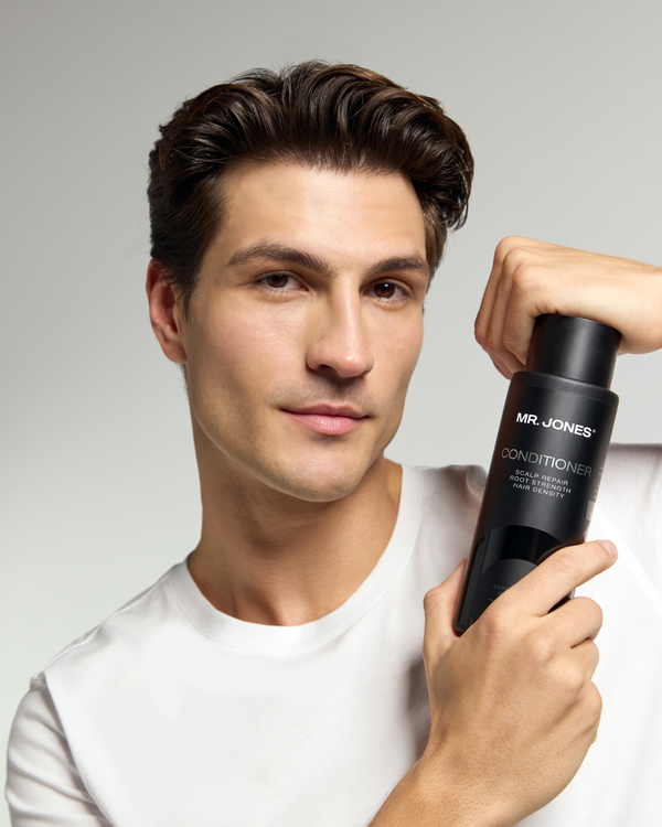 Man holding a bottle of 'Mr. Jones Conditioner' conditioner against a grey background