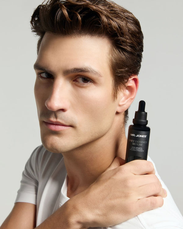 Man holding a black bottle labeled 'Mr. Jones Grey Defence Serum' against a grey background