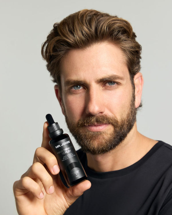Man holding a black dropper bottle 'Hair Density Serum' with a grey background