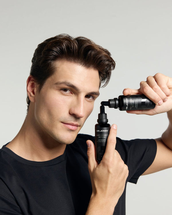 Man holding two black bottles with droppers against a gray background