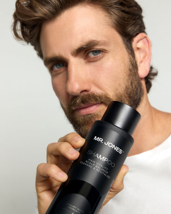 Man holding a black shampoo bottle labeled 'MR. JONES' against a neutral background