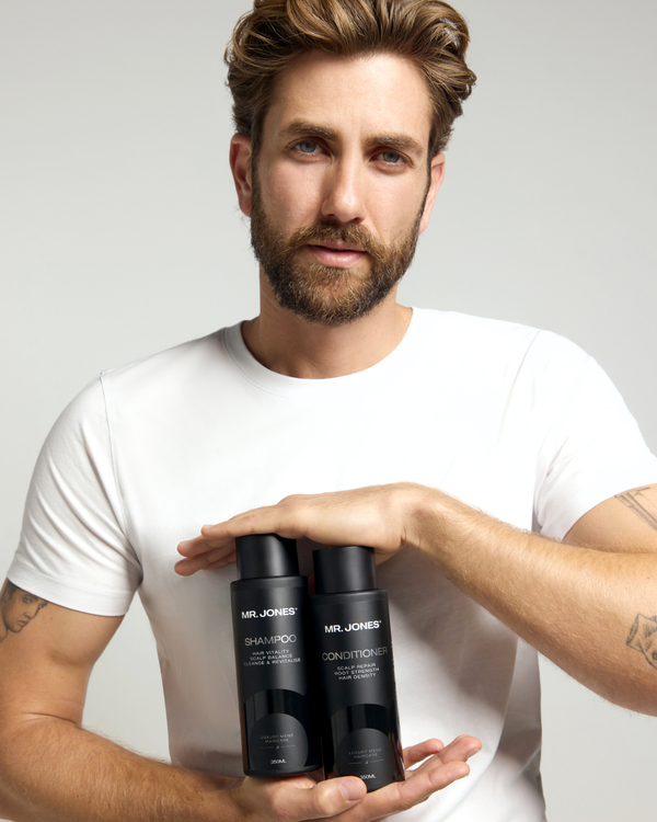 Man holding two black bottles labeled 'Mr. Jones Shampoo and Conditioner' against a light grey background