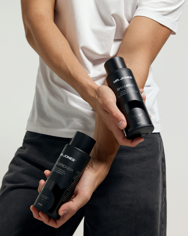 Person holding two bottles of Mr Jones hair care products against a plain background