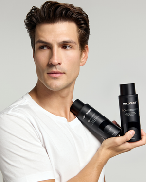 Man holding two bottles of 'MR. JONES Shampoo and Conditioner' hair care products against a grey background