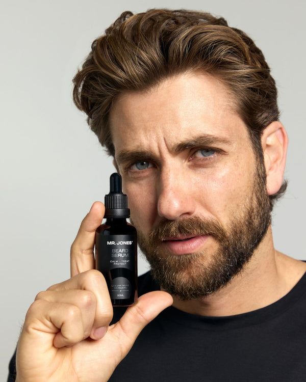 Man holding a bottle of Mr. Jones Beard Serum product against a grey background