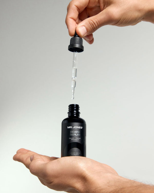 Hand holding a dropper bottle of Mr. Jones Beard Serum with a grey background