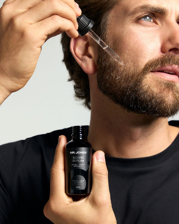 Man applying beard serum from a dropper bottle to his beard.