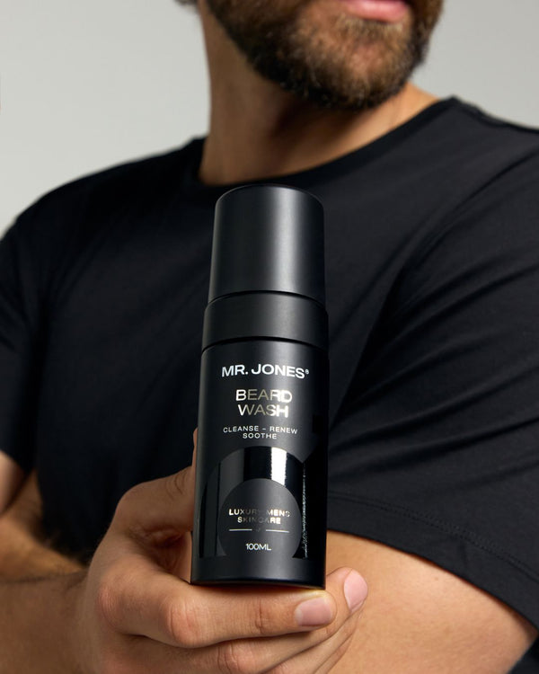 Person holding a black bottle of 'Mr. Jones' beard wash against a neutral background
