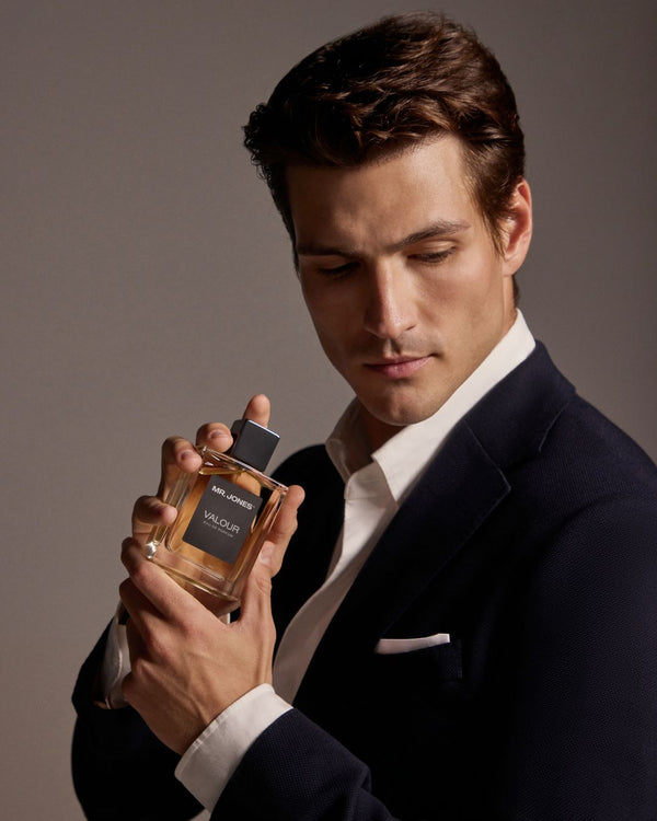 Man holding a perfume bottle with a grey background