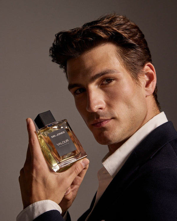 Man holding a perfume bottle labeled 'Valour' against a neutral background