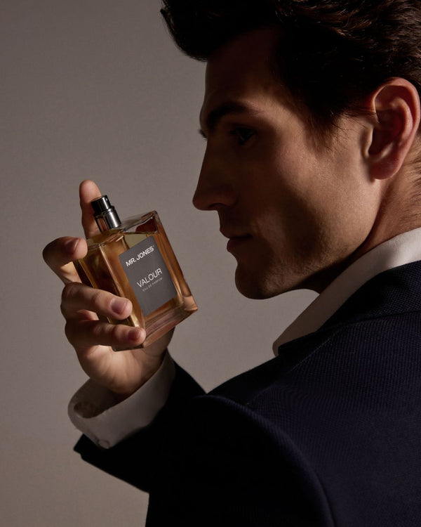 Man holding a perfume bottle labeled 'Valour' by Mr. Jones against a neutral background