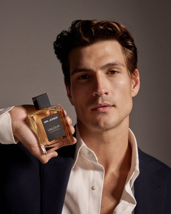 Man holding a perfume bottle labeled 'Valour' against a neutral background