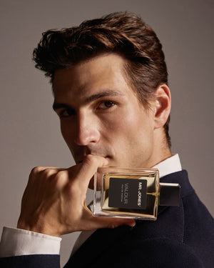 Man holding a perfume bottle labeled 'Valour' against a neutral background