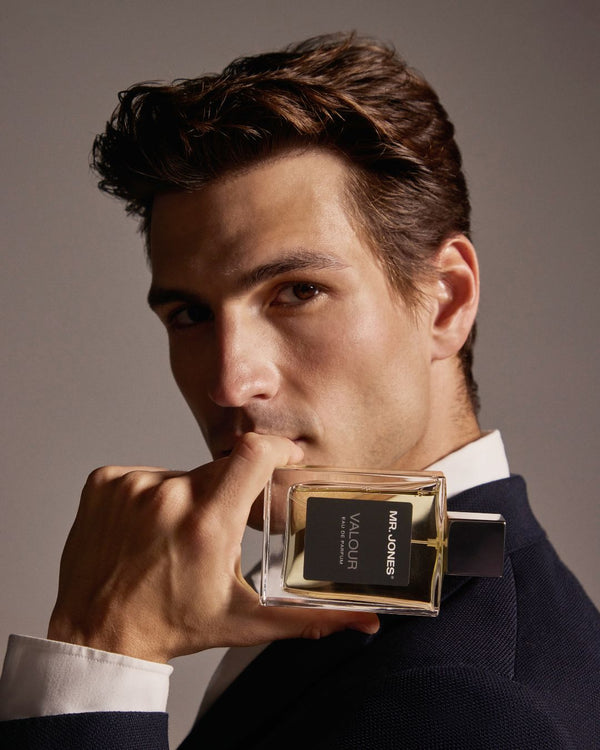 Man holding a perfume bottle labeled 'Valour' against a neutral background